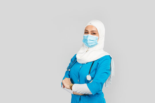  Friendly Muslim Doctor Or Nurse Wearing Hijab And Medical Face Mask And Gloves On A Gray Background.