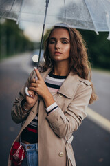 Naklejka premium Portrait of a beautiful young woman with umbrella under the rain at the autumn, outdoors.