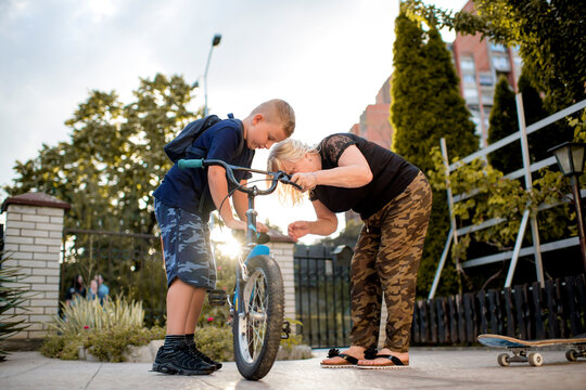 Grandmother helping young boy to fix bike outdoors in garden