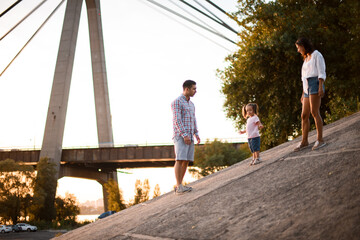 Father and mother walks with little daughter in pink t-shirt on summer day