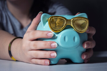 A woman holds a piggy Bank with gold glasses. Close up