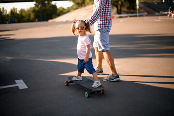 Close-up view of little girl riding skateboard while her father walks beside