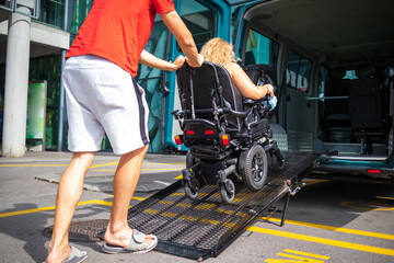 Woman on wheelchair using a vehicle ramp. Accessible transport with assistant driver.