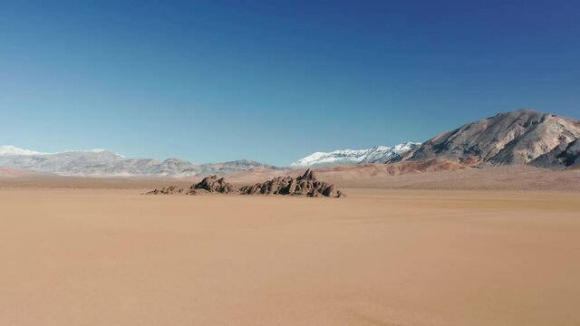 Cinematic wild pure nature. Flying toward dark stone island on the ancient dry lake bed of desert. Beautiful 4K aerial of empty landscape. Scenic outdoor adventure to Race Track playa, Death Valley