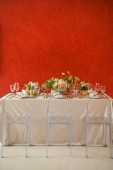 Elegant table setting with gold accents and red wall, clear chairs and flowers