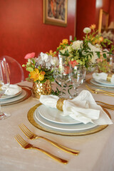 Elegant table setting with gold accents and red wall, clear chairs and flowers