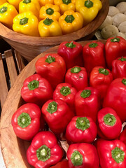Vibrant display of fresh red and yellow bell peppers arranged in wooden bowls. The peppers are neatly organized, with the green stems facing upward, creating a colorful and appetizing presentation.