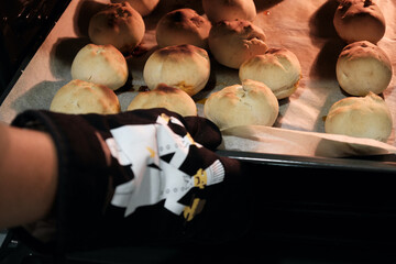 Person with kitchen mittens taking out some buns on a baking tray