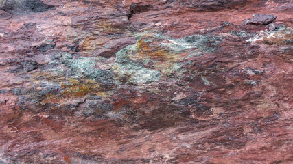 Background from red jasper with bright splashes of purple, turquoise and orange mineral. Stone texture of gabbro diabase. Boulders from red jasper in landscape design.