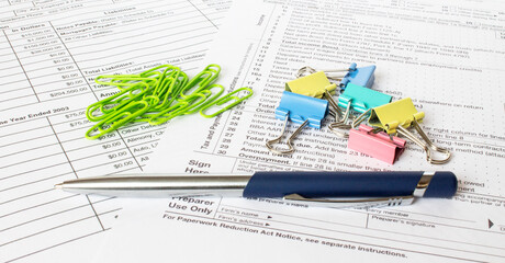 A blue metal pen sits on the financial tables with multi-colored stationery clips