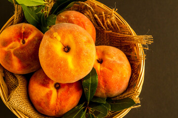 Fresh, ripe peaches in a wicker basket on dark surface with copy space,above view