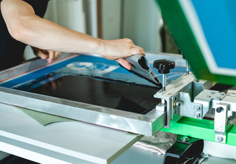 Cropped view of man holding squeegee while applying plastisol ink on stencils on screen printing...