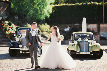Wedding couple, beautiful bride and elegant groom holding hands and looking at each other near retro wedding car