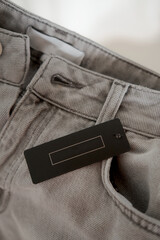 Clothing tag in black color on gray jeans fabric. Fashion brand name mock up