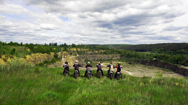 Enduro racers sitting on motorcycles near the abyss, watching the sunset.