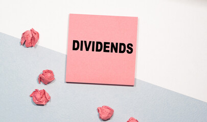 DIVIDENDS the inscription on the pink sticker, next to scattered crumpled papers. white-and-blue background. Business concept