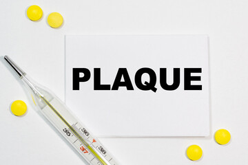 PLAQUE text written on a white business card next to yellow tablets and a thermometer. Medical concept.