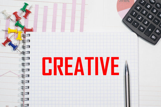 CREATIVE inscription on a notebook against the background of calculator charts, paper clips and pens