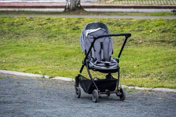 empty gray stroller on the road against the background of the lawn