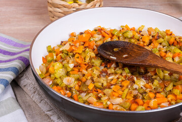 Cooking fried vegetable base for carrot and celery onion dishes - ready-made mirepoix or soffritto in a pan, top view, close-up.