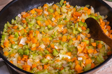 Cooking fried vegetable base for carrot and celery onion dishes - ready-made mirepoix or soffritto in a pan, top view, close-up.