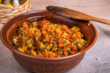 Fried vegetable bases for carrot and celery onion dishes - mirepoix or soffritto in a clay bowl on a wooden table, rustic style, close-up
