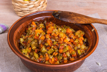 Fried vegetable bases for carrot and celery onion dishes - mirepoix or soffritto in a clay bowl on a wooden table, rustic style, close-up