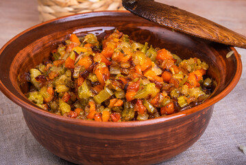 Fried vegetable bases for carrot and celery onion dishes - mirepoix or soffritto in a clay bowl on a wooden table, rustic style, close-up