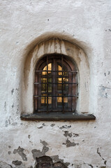 Tiny caged old window in bleached monastery wall