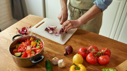 Close up of hands of man, chef cook cutting onion on the chopping board while preparing a meal in the kitchen