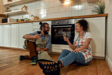 Young happy couple having glass of wine while cooking in the kitchen. Man and woman in apron waiting for pizza to be cooked