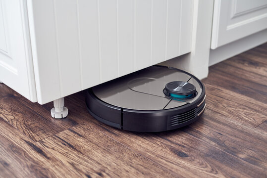 Close up of Robotic vacuum cleaner on laminate wooden floor cleaning under the closet. Smart cleaning technology. Selective focus with copy space