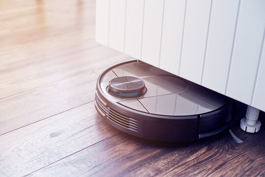 Close up of Robotic vacuum cleaner on laminate wooden floor cleaning under the closet. Smart cleaning technology. Selective focus with copy space