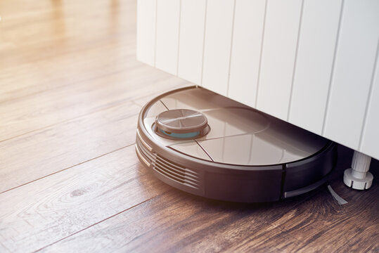 Close up of Robotic vacuum cleaner on laminate wooden floor cleaning under the closet. Smart cleaning technology. Selective focus with copy space