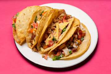 Mexican hard-shell tacos with meat and fresh sauce on pink background