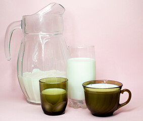 Natural whole milk in a jug and a glass isolated on a pink background closeup