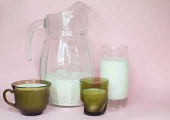 Natural whole milk in a jug and a glass isolated on a pink background closeup