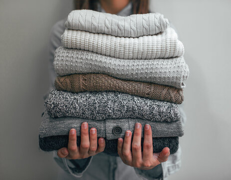 Woman holding a stack of winter wool sweaters.