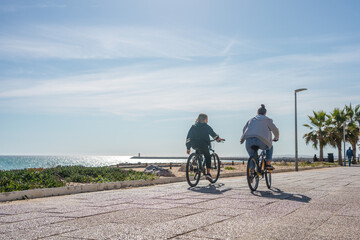 Bicyclists riding along the beach sunshine blue sky outdoors background, person back view.
