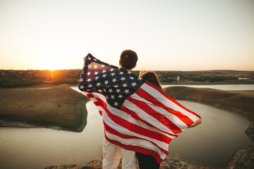 Happy couple with the American flag in mountain at sunset. Independence Day celebration.