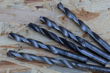 Five metal drills of the same diameter lie on a wooden background.