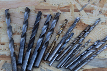 Metal drills of different diameters lie on a wooden background.