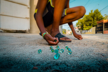 brown-skinned boy playing marbles in the streets of the neighborhood