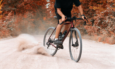 Fototapeta na wymiar Сyclist on bike rides along the gravel road raising dust from the rear wheel in autumn forest. Gravel biking. Extreme sports and activity concept.