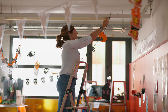 Female teacher on a ladder decorating a halloween corner at school