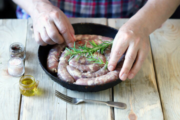 Selective focus. A male chef is putting raw sausages in a frying pan.