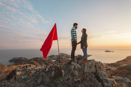Young couple looking at each other with red flag in a cliff.
