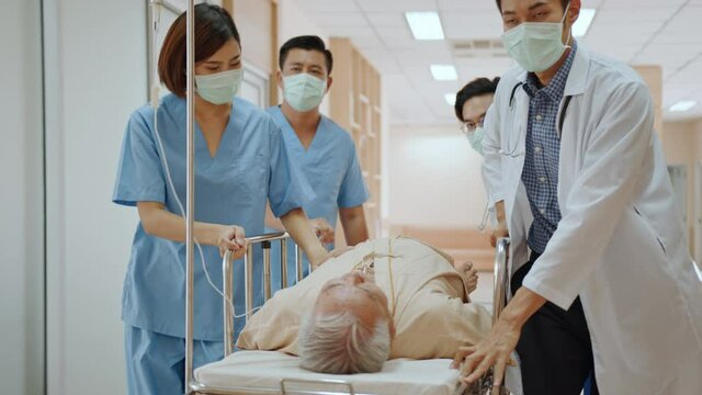 Group of Asian emergency doctor and nurse team wear face mask, push emergency stretcher, transport senior patient in hospital. Health care paramedic service, or medical rescue team operation concept