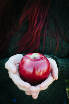 A redheaded woman holding a red apple