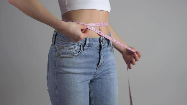 Slim woman in blue jeans measuring her perfect waist after successful weight loss